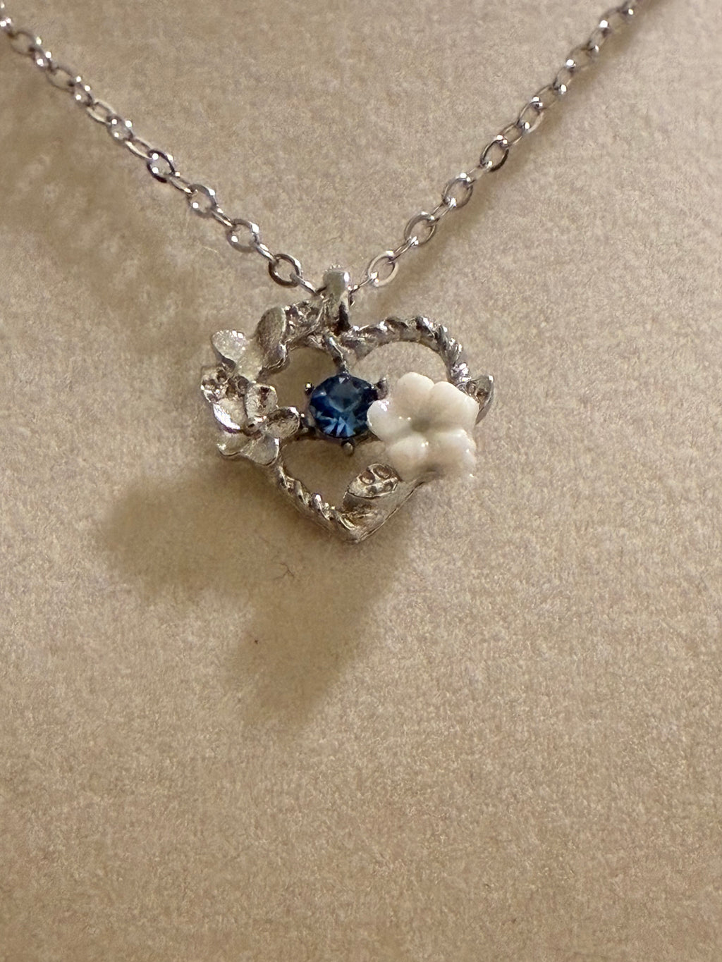 Silver plated heart pendant with a blue stone and white floral charm
