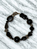 chunky black gemstone toggle bracelet, featuring mixed shapes of polished black stones like onyx or obsidian accented by decorative metallic spacer beads.