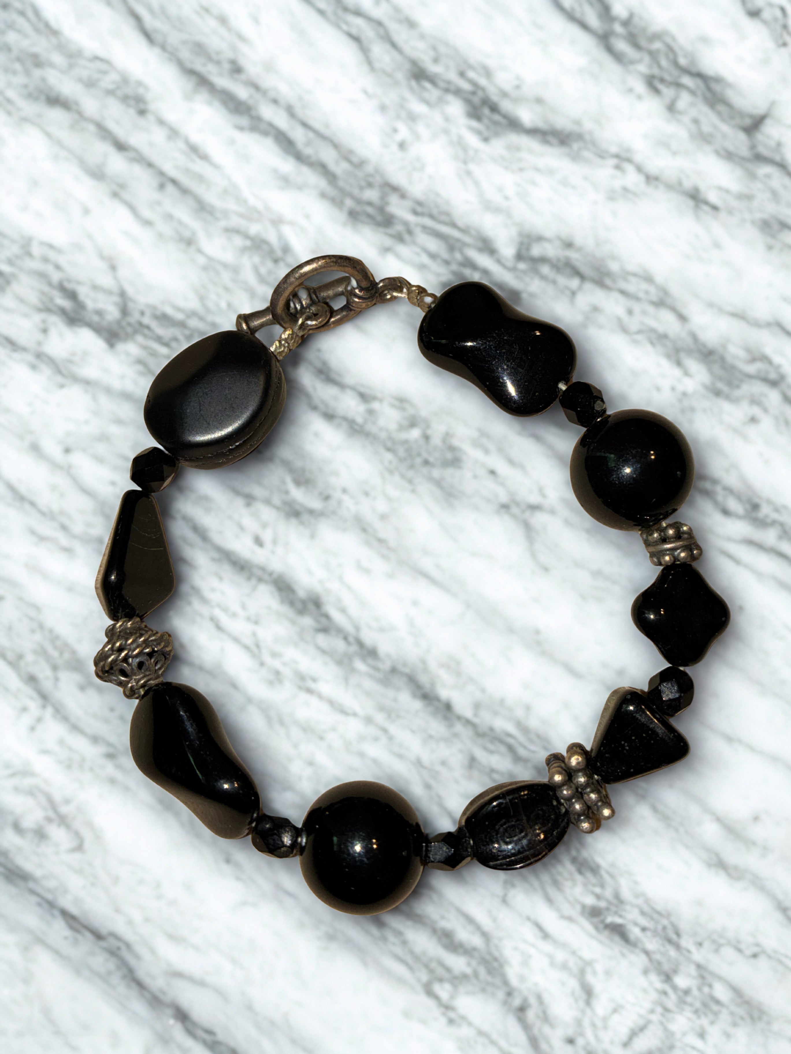 chunky black gemstone toggle bracelet, featuring mixed shapes of polished black stones like onyx or obsidian accented by decorative metallic spacer beads.